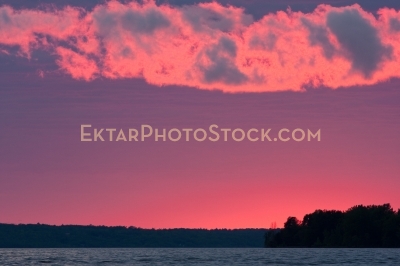 Red glowing sunset with clouds and shore line with trees